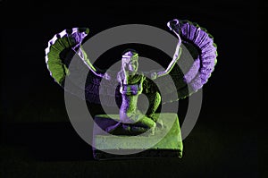 Closeup to a Isis. female old winged egyptian god mini figurine iluminated with green and violet lights photo