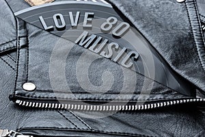 Closeup to a love 80 music lettering art over a black leather biker jacket with LP vinyl disc