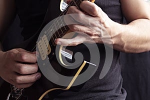 Closeup to a man wearing a black t-shirt playing a black and yellow electric guitar with wooden background