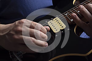 Closeup to a man wearing a blue navy t-shirt playing a black and yellow electric guitar with wooden background