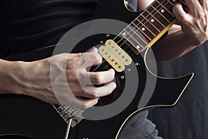 Closeup to a man wearing a leather jacket playing a black and yellow electric guitar with black background