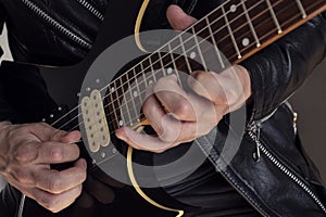 Closeup to a man wearing a leather jacket playing a black and yellow electric guitar with black background