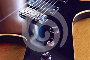 Closeup to a six black electric guitar strings, bridge and volumen and tone controls over a wooden table photo