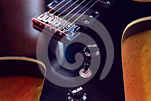 Closeup to a six black electric guitar strings, bridge and volumen and tone controls over a wooden table photo