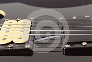 Closeup to a six black electric guitar strings, wooden fretboard and microphones