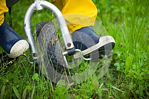 Closeup of toddler child feet in rubber boots and pants riding a bicycle on green grass. Boy walking outdoors