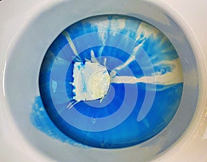 Closeup of toilet bowl seat with blue white environmantal harmful chemical chlorine aggressive cleaning detergent product