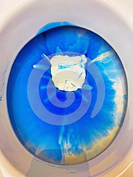 Closeup of toilet bowl seat with blue white environmantal harmful chemical chlorine aggressive cleaning detergent product