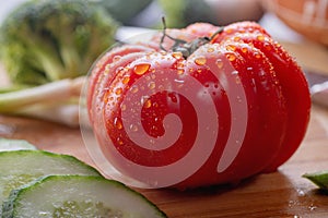 Closeup tomato with water drops and green cucumber and onions