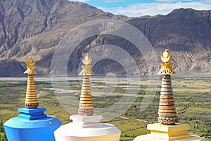 Closeup top of three colorful religious stupas with mountain view.