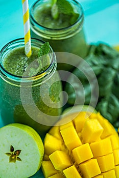 Closeup top view of green smoothie with mango, apple, spinach in glass jars. Turquoise blue table