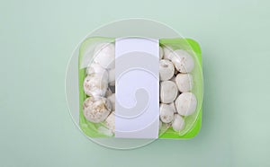 Closeup and top view of packaged white mushrooms in the box on the bright green surface.Blank tag for price