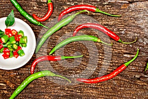 Closeup and top view red and green chili with chili sliced in a white ceramic mini bowl on wooden background