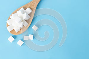 Closeup top view sugar cubes on wooden spoon white blue background