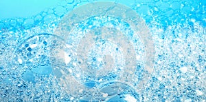 Closeup of transparent bubbles of soap foam covering surface of bright blue water