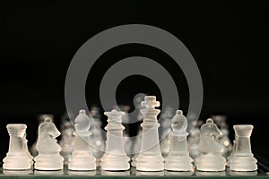Closeup of transparent chess pieces on a board against a dark background