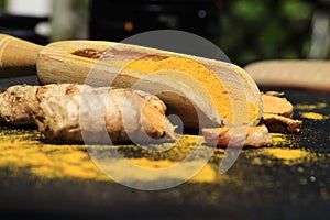 Closeup of turmeric powder on a wooden spoon and roots on a dark table