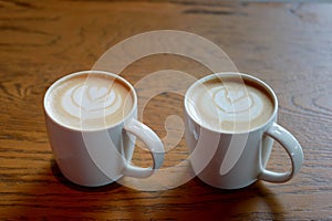 Closeup twin Latte art fresh coffee in the white cup with white milk foam heart on top on the wooden table background.