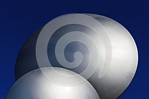 Closeup of two abstract isolated metallic silver colored shiny round sphere discs against dark deeep blue sky