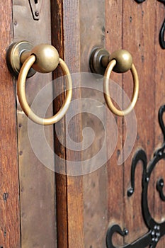 Closeup of two antique copper ornate door knockers over an aged wooden door.