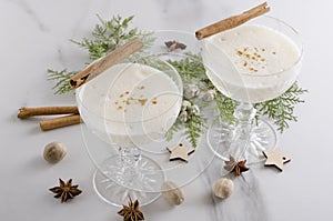 Closeup of two cocktail glasses of aromatic tasty eggnog with alcohol, cinnamone sticks, nutmeg.Delicious traditional Christmas dr photo