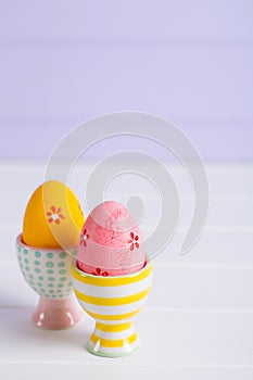 Closeup two colorful painted Easter eggs in vibrant modern egg stands on pastel lilac background