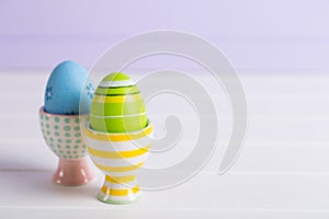 Closeup two colorful painted Easter eggs in vibrant modern egg stands on pastel lilac background