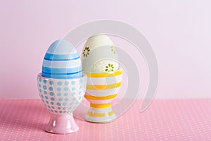 Closeup two colorful painted Easter eggs in vibrant modern egg stands on pastel pink background