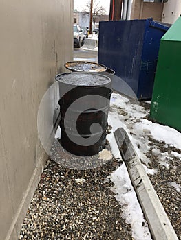 Closeup of two dirty greasy barrels outside building with garbage and recycling bin.