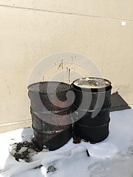 Closeup of two dirty greasy barrels outside building in snow.