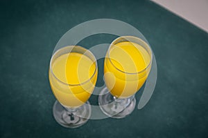 Closeup of two glasses of orange juice on a blurry green background