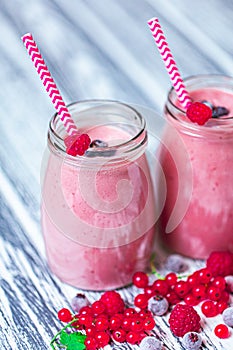 Closeup two jars of yogurt smoothie with cranberry, raspberry, blueberry on wood table.