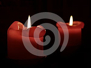 Closeup of two red candles burning on a dark background