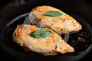 Closeup of two whole chicken breasts roasting in cast iron pan. Bay leaf garnish