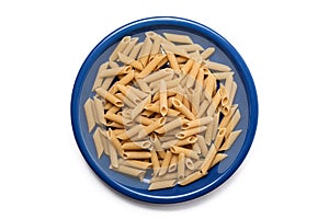 Closeup of uncooked organic penne rigate pasta in blue plate on white background. Slow carbs concept. Top view