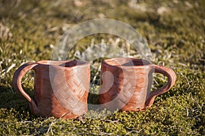 Closeup of unique handmade two cups with folk signs on green moss in summer sunset sunlight before kiln