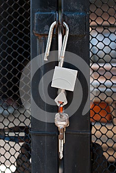 Closeup, unlocked silver padlock hanging on the black iron door.