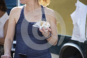 Closeup of unrecognizable girl in sleveless teeshirt with exercise wristband eating food from food truck outdoors photo