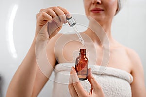 Closeup of unrecognizable woman in white towel holding small bottle with beauty product, applying nourishing, anti-aging,