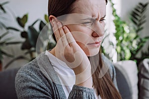 Closeup up side profile of sick young caucasian female having ear pain touching painful head sitting on sofa. Unhealthy woman 20s