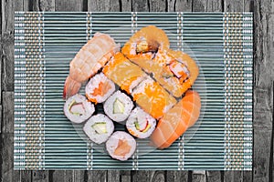 Closeup of various kinds of sushi rolls with salmon, sashimi and other slices of raw fish served on a green bamboo mat on rustic