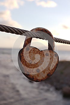 Closeup vertical shot of a rusty weathered heart-shaped padlock hanging from a rope