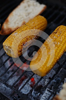 Closeup vertical shot of salted corn grilled next to bread on the grates outdoors