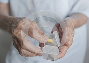 Closeup view of aged senior asian woman taking Pills from white colored transparent plastic medicine box.