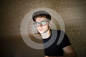 Closeup view of bearded young businessman in eyeglasses working at office at night man using laptop. Hacker