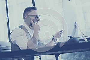 Closeup view of bearded young businessman wearing white shirt,waistcoat and working at the desktop computer in modern