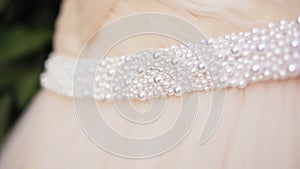 Closeup view of beautiful wedding dress with pearls hanging on the tree branch. Slowmotion shot