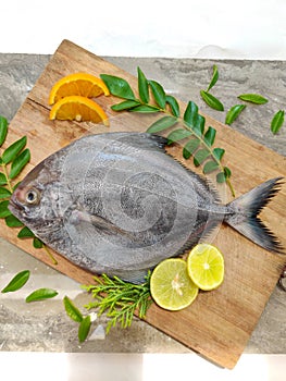 Closeup view of black pomfret fish decorated with fruits and herbs on a wooden background,Selective focus photo