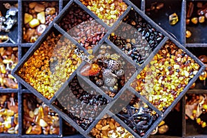 Closeup view at a black tray for handcrafting with multiple sections filled with various kinds of amber and tools for crafting