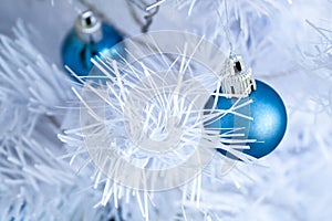 Closeup view of a blue matte ball hanging on a silver thread on a white artificial Christmas tree for a family holiday